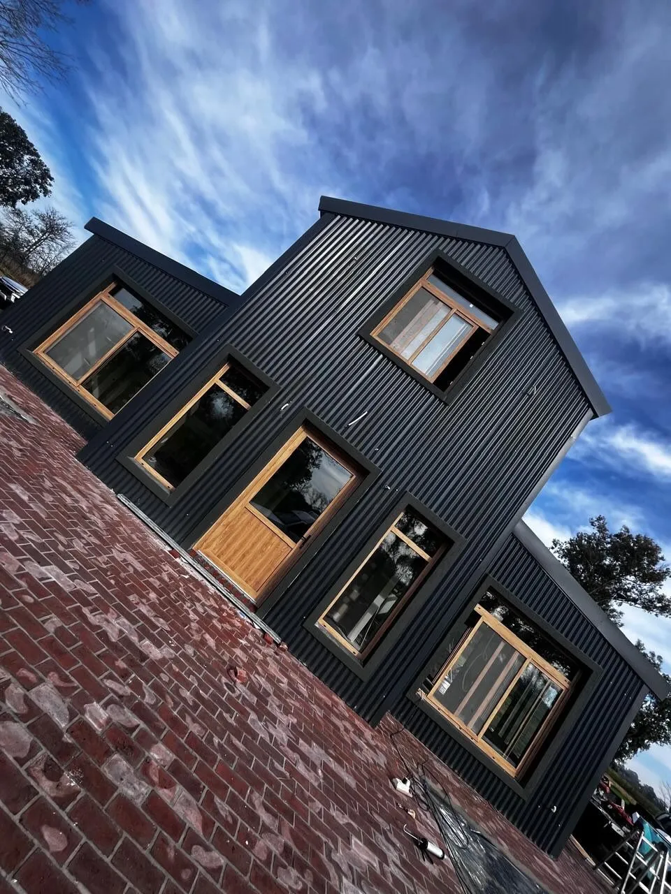 Fachada de chapa negra en Lincoln con ventanas y puerta de PVC roble dorado