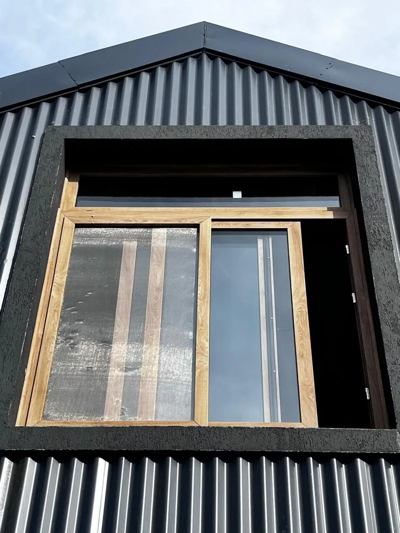 Ventana corrediza de PVC roble dorado con banderola fija en el hastial de la casa