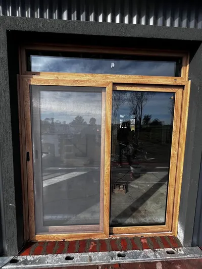 Ventana corrediza de PVC roble dorado con mosquitero y paño fijo superior