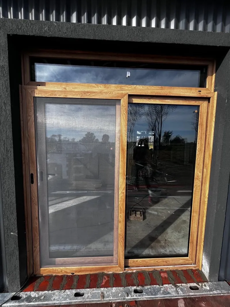 Ventana corrediza de PVC roble dorado con mosquitero y paño fijo superior