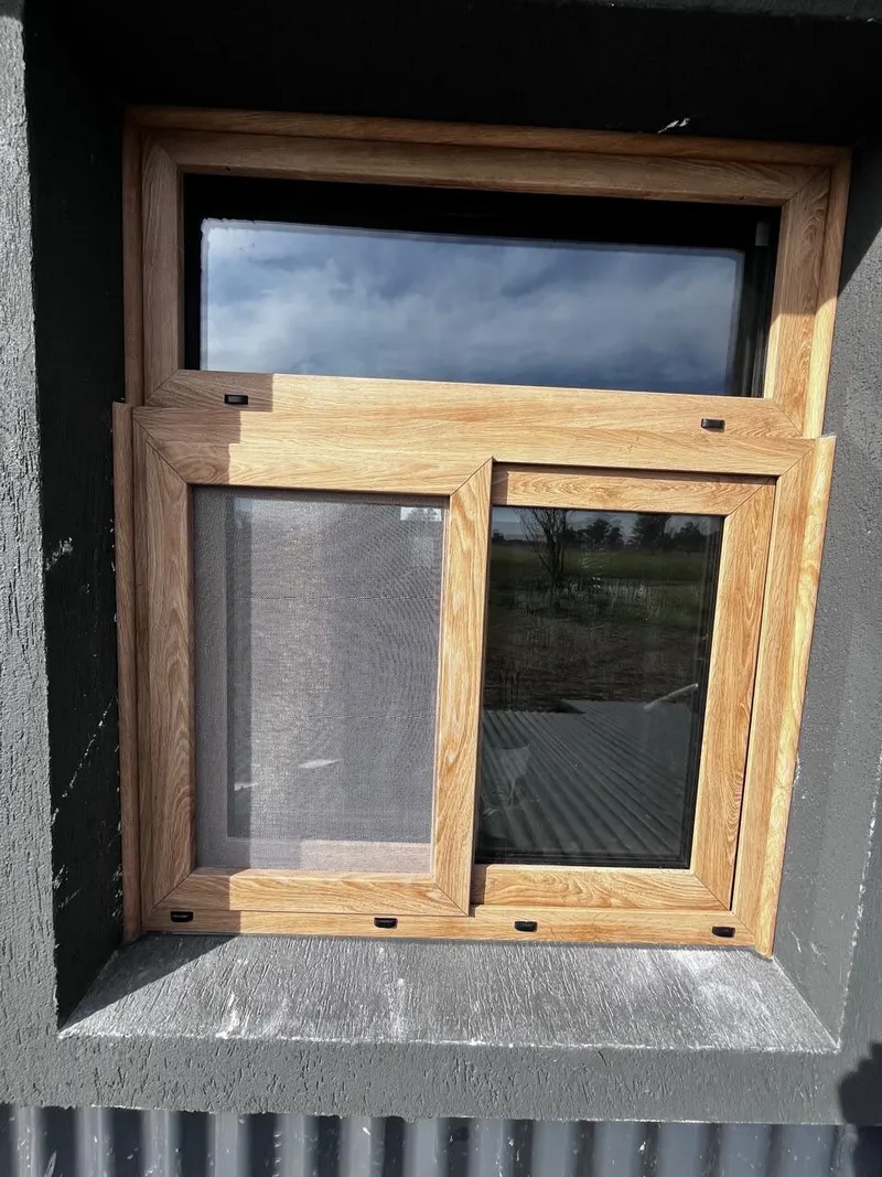 Detalle de una ventana corrediza de PVC roble dorado con mosquitero