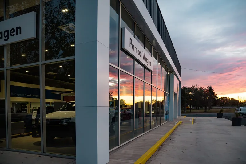 Lateral del concesionario con piel de vidrio y perfilería de aluminio al atardecer