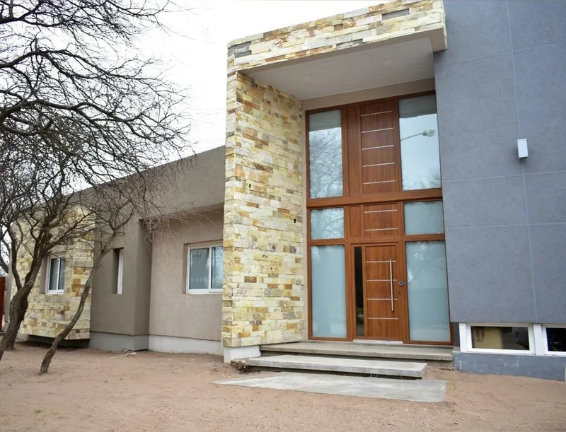 Acceso de la casa con puerta de PVC roble dorado entre el revestimiento de piedra y el frente gris