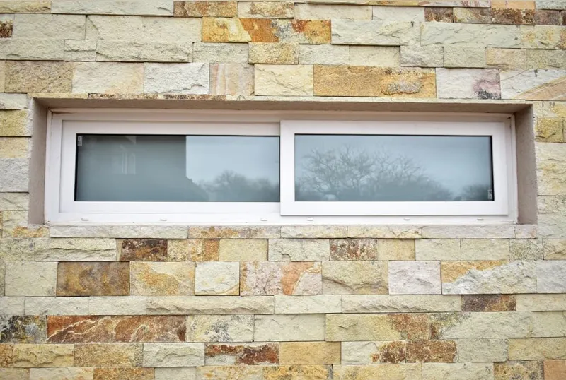 Ventana apaisada corrediza de PVC blanco integrada al revestimiento de piedra