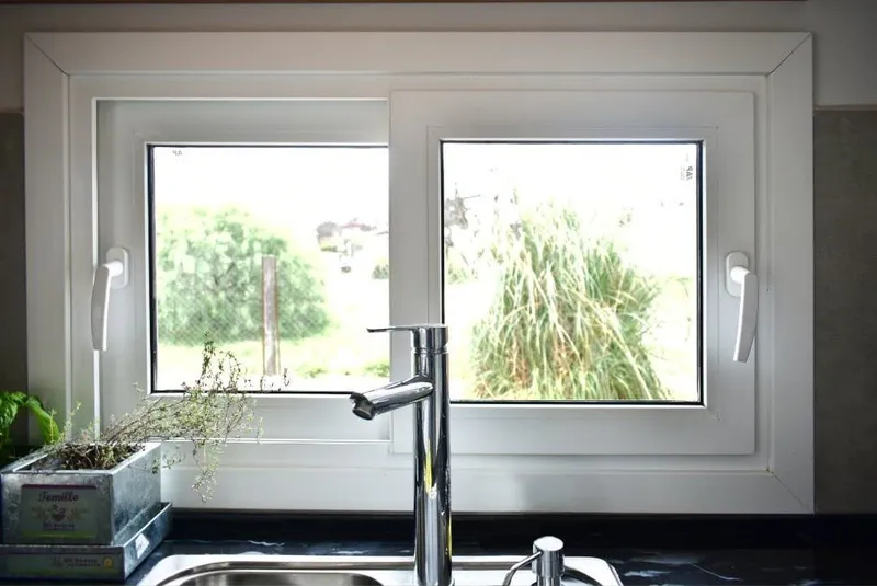 Ventana de dos hojas oscilobatientes de PVC blanco sobre la bacha de la cocina