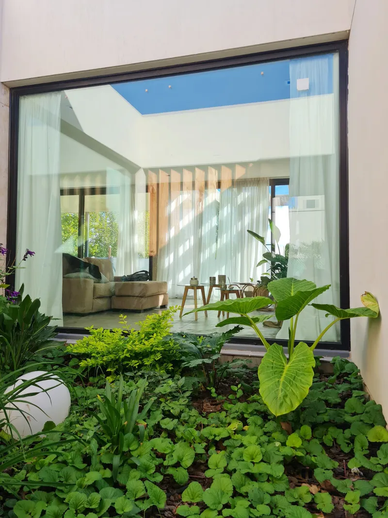Vista del living a través de los paños fijos de aluminio negro del patio