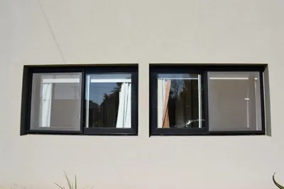 Dos ventanas corredizas de aluminio negro en la fachada de la vivienda