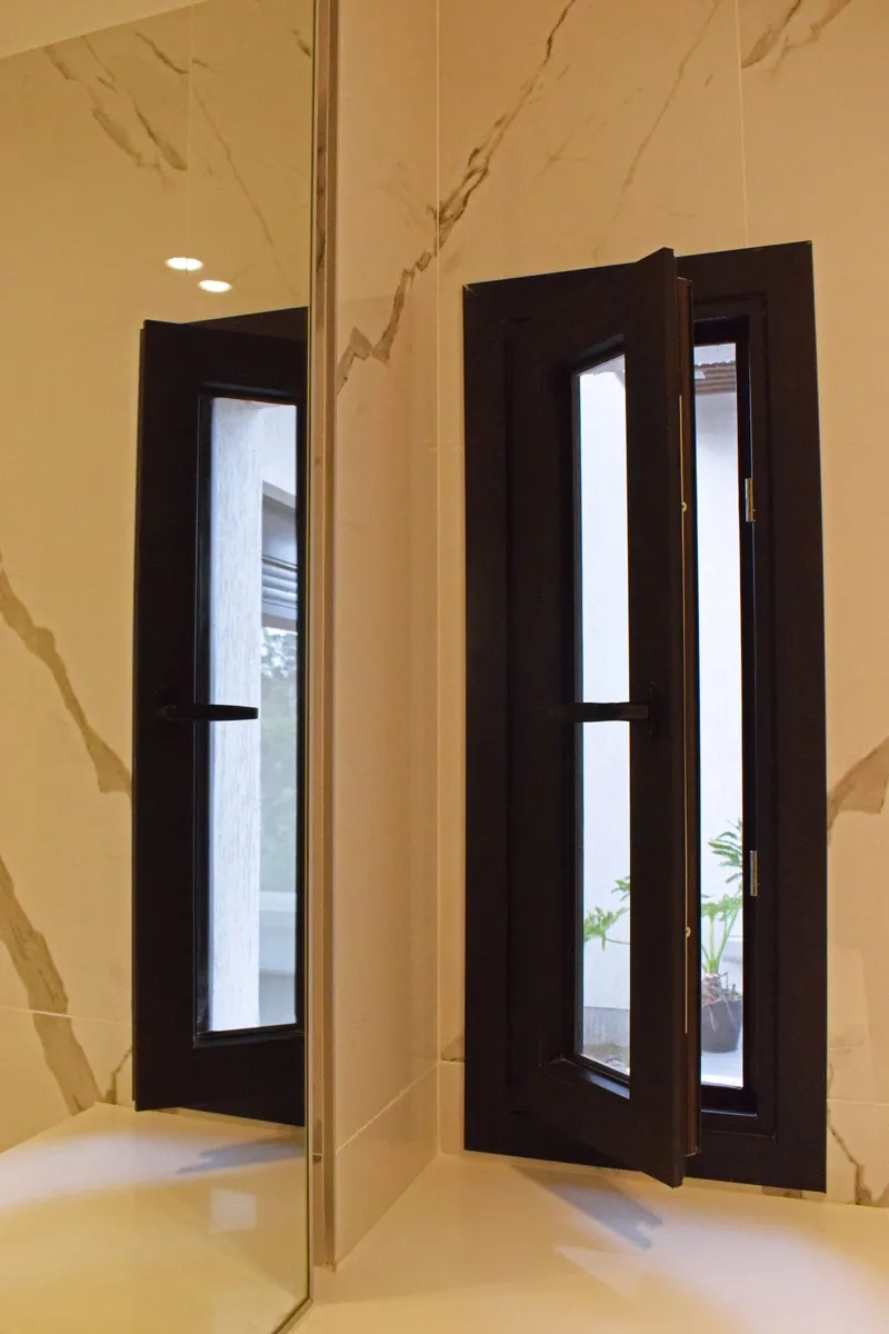 Puerta de PVC negro con paño vidriado vertical, reflejada en el revestimiento de mármol