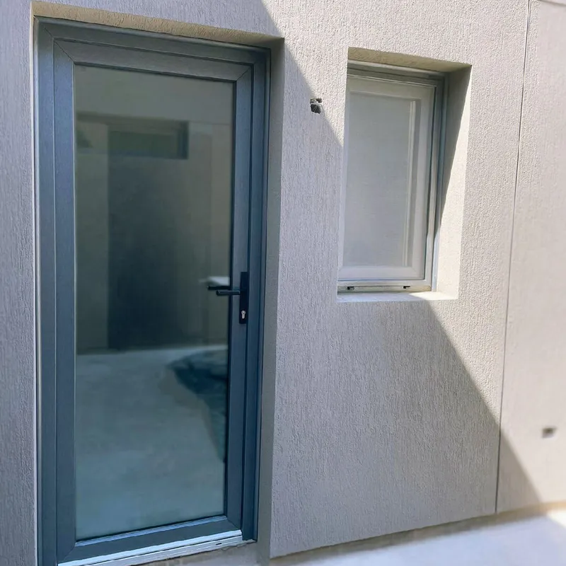 Puerta de PVC Titanio vidriada y ventana de PVC blanco en el lateral de la casa